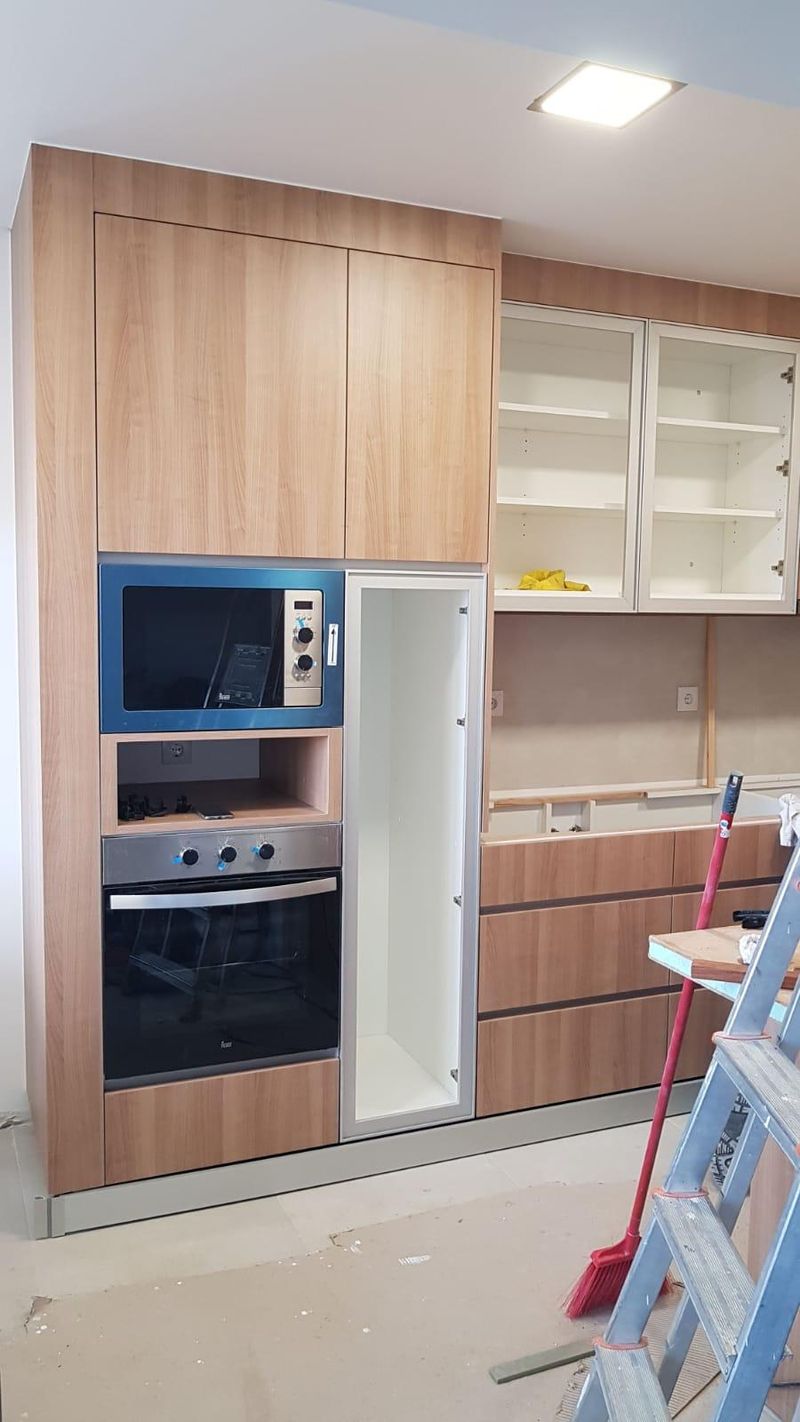 Coluna com micro-ondas e forno ao lado de uma vitrine com prateleiras, durante a obra.